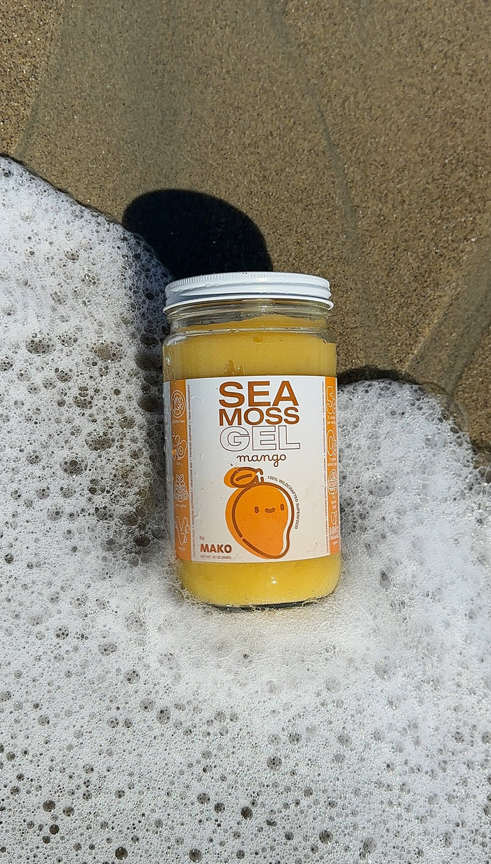 Mako Vitality Mango sea moss gel in a glass jar on a sandy beach at the water's edge