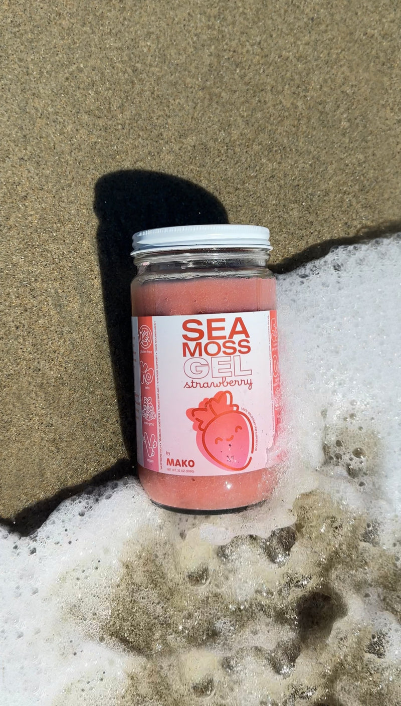 Mako Vitality Strawberry sea moss gel in a glass jar on a sandy beach at the water's edge
